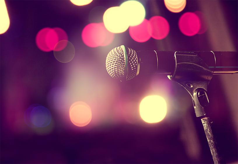 A microphone and microphone stand with blurred out spotlights behind it.