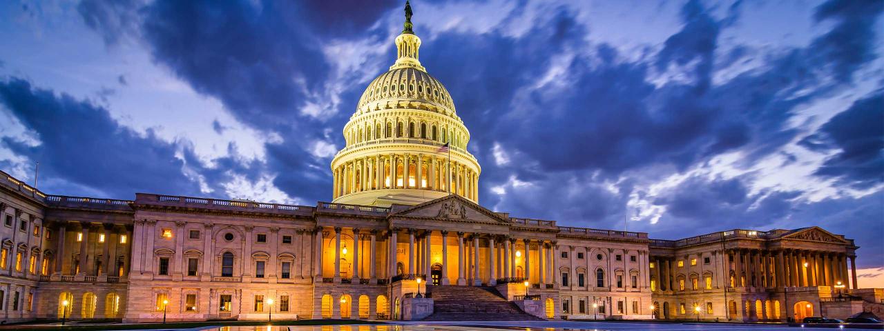 Image of the capitol building with a dusk sky with clouds and lights on the building.