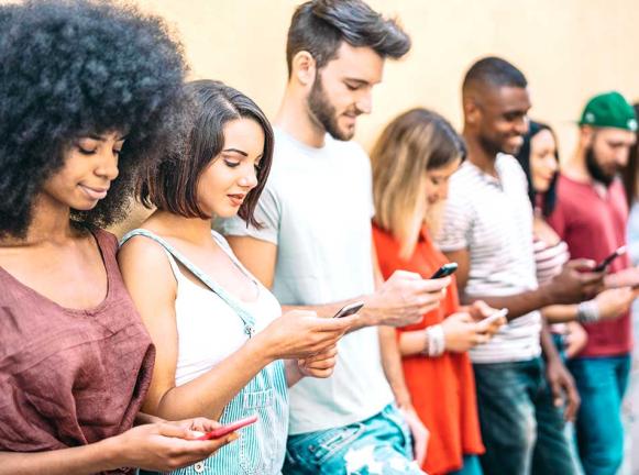 Imagen de adolescentes de pie contra la pared mirando teléfonos celulares