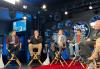 Crabtree-Ireland, seated second from left, speaks. He wears a black jacket with SAG-AFTRA’s logo and khaki pants. Other panelists are visible. The studio has bright lights, KNX’s logo, and a red carpet on the floor.