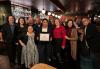A large group in individuals in a restaurant/bar space. A man in the center front row, Asian American, holds up a framed certificate.