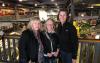 From left, Nordstrand, Howell and West take a photo inside an industrial-like setting. Their clothing is casual; Nordstrand wears a distinctive checkered scarf with flowers. West is significantly taller. Behind them are various types of machinery.