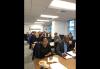 A grouop of seated individuals at desks with pen and papers. A group of seated individuals at desks with pen and papers.