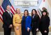 Five individuals take a photo inside a governmental office. Behind them are the American and California state flags and an image of the California State Capitol building.