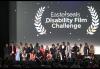 A large, diverse crowd gathers onstage in a theater. Behind them on a large projector is a title card for the 2024 Easterseals Disabilities Film Challenge.