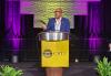 SAG-AFTRA Vice President, New York Ezra Knight delivers a keynote address at the Coalition of Black Trade Unionists 53rd Annual Convention on May 23. Knight (Black) is captured mid-speech on stage behind a podium bearing the Coalition of Black Trade Unionists’ name and logo. He wears a blue blazer and a light-colored dress shirt. He is framed by two fern plants and the lighting behind him is purple.