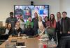Members of the DFW and Houston-Austin Locals pose for a photo with acting coach Ransford Doherty. Attendees pose for a photo in front of a screen showing those who are attendning via Zoom. Some members sit at a table that has various items on it.