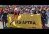 L.A. Local SAG-AFTRA members attend International Workers’ Day with a march and rally in Hollywood on May 1. A large group of people of different ethnicities pose with a yellow SAG-AFTRA banner outside. Many wear SAG-AFTRA or "SAG-AFTRA Strong" T-shirts.