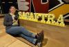 Local member Sophie Craft strikes a pose at the New England NextGen event. Craft, in jeans and a brown jacket, sits on the floor holding a small bowling ball in front of a lighted sign that spells SAG-AFTRA.
