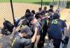 The SAG-AFTRA softball team huddles in the dugout before the game starts. A group of men in black and yellow SAG-AFTRA jerseys huddle together in the dugout.