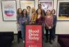New York Health Care Safety Net Committee members and volunteers, Rachel Lynn Jackson, Slawa Khan, Carrie Gibson, Blood Drive Subcommittee Chair Cherokee Black, Committee Chair Cathy Lilly, J.R. Carter, Tania Villanueva and Elizabeth Cappuccino. Seven women and one man stand in the SAG-AFTRA New York office behind a sign that reads "Blood Drive Today." There are four posters for SAG-AFTRA and the SAG-AFTRA Foundation on the wall behind them.