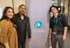 SF-NC Local member and APAM Committee member Rajiv Shah, center, with wife and content creator Kim Ocampo-Shah and Center of Asian American Media Development & Partnerships Manager Jonathan Hsieh at the CAAMFest Opening Night Gala May 9. From left, Ocampo-Shah, Shah and Hsieh in a lobby-like setting. They frame a standing banner for the Center of Asian American Media, which shows its logo, an abstract drawing of interconnected circles in shades of blue and white, and copy “CAAM” in white.