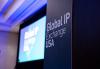 An atmospheric shot from the event floor. In the foreground is a black rectangular structure with “Global IP Exchange” written on the front in large white letters. In the background is a projection screen with the event’s title card. The screen is slightly blurred, but the words “Global IP Exchange USA” are decipherable.