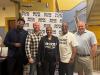 Five individuals, four men and one woman, stand in the lobby of a building. The woman and a man, second from right, both wear T-shirts that read "Rox Film" in all caps. Behind the group is a white step-and-repeat backdrop with the film festival logo.