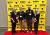 Four individuals on the red carpet in a nondescript room. Behind them is a yellow step-and-repeat backdrop with the SXSW logo.