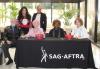 The L.A. Local Host Committee welcomes SAG-AFTRA members to the 2024 Los Angeles Local Holiday Open House. Six individuals sit and stand behind a black “SAG-AFTRA” tablecloth.