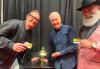 Three individuals take a photo backstage. Gleason wears a black bomber jacket over a black shirt and light-colored pants, and Morgan wears a pink-patterned blazer, a black dress shirt and tie, and a black cowboy hat. Gleason and Morgan hold their SAG-AFTRA membership cards. On a table beside Daniels is a small CP30 figurine that holds his member card.