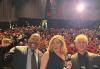 From left, Knight, Hammel and Baron are in the foreground. Knight raises his right fist. Behind them is a crowd seated in theater chairs. In the upper right corner is a glare from the projector.