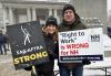 SAG-AFTRA members Duncan Putney and Chelsea Heuter in front of the New Hampshire Capitol Building in Concord holding signs that read “SAG-AFTRA Strong” and “Right to Work Is Wrong for NH.” Two SAG-AFTRA New England Local members pose for a photo outside of the New Hampshire State Legislative Building. Both wear SAG-AFTRA hats and winter jackets and hold signs rallying against passing right-to-work legislation in the state.