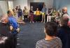 Certified Alexander Technique teacher Katie Beckvold opens the New England Winter Actors Academy with a group activity. A large group of diverse people gather in a circle in the SAG-AFTRA New England Local’s conference room, one member holding a yellow ball while they prepare for an acting exercise.