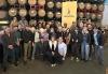 Photo: SAG-AFTRA members from the New Orleans Local stunt community at a social gathering. A large group of people pose for a photo in front of a stack of barrels and a yellow SAG-AFTRA banner.