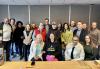 Los miembros del Local de Filadelfia asisten a la reunión de capacitación de liderazgo el 16 de noviembre en el Courtyard Philadelphia City Avenue para discutir las prioridades y planificar el calendario local 2025. Un grupo diverso de personas posa para una foto detrás de una mesa de conferencias y frente a una pared gris al final de una reunión.