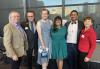 From left, Steve Reeder, Rik Deskin, Ry Armstrong, Seattle Local President Deborah Horne, Shobhit Agarwal and Rachel Glass. Six people stand closely together for a photo in front of a building. The city can be seen reflected in the windows behind them.