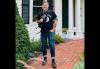 Minnesota Public Radio Reporter Jon Collins A man wearing blue jeans, boots and a black T-shirt holds a microphone while standing on a red brick sidewalk outside of a white wooden building.
