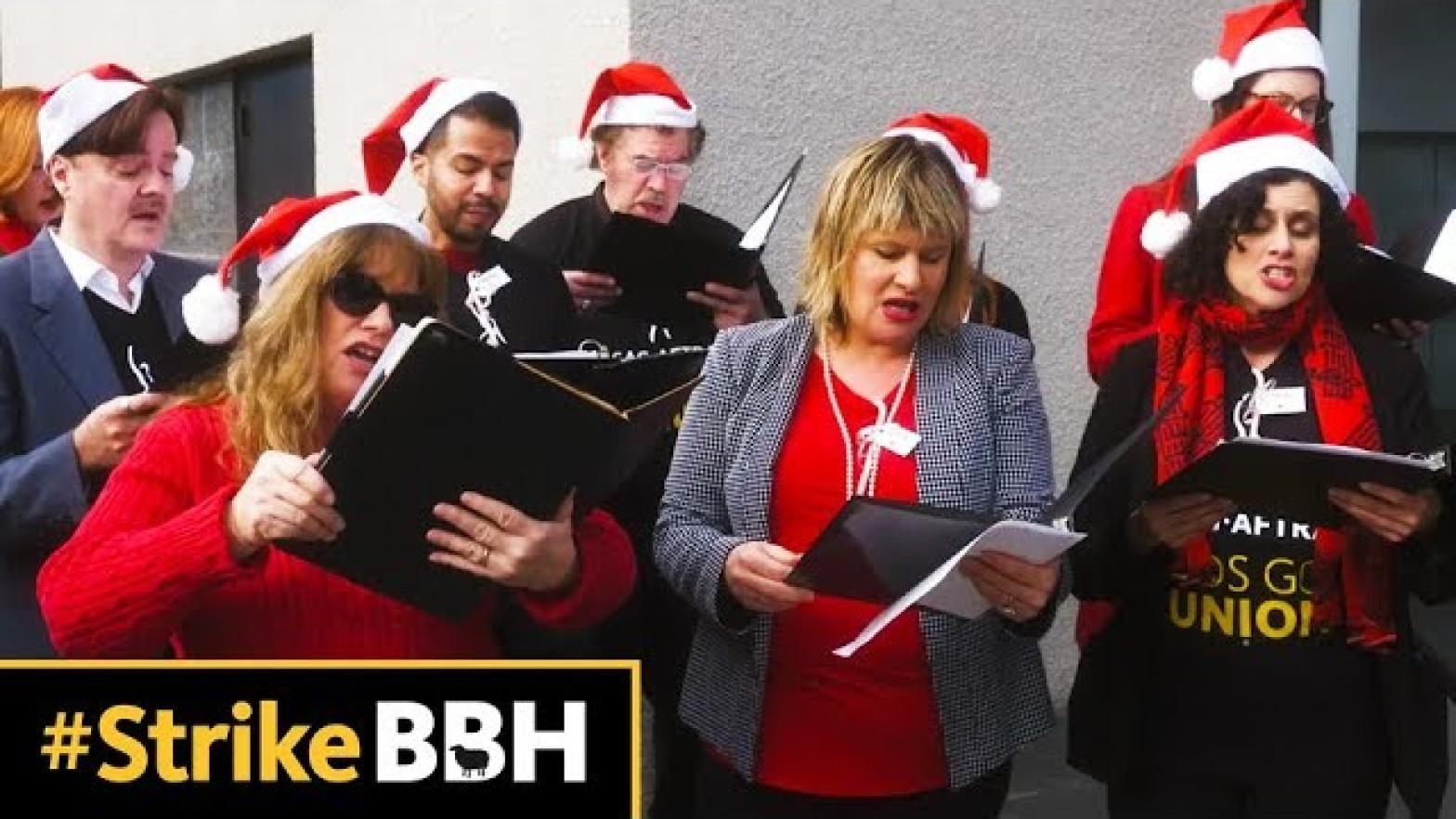 members holding binders in front of them wearing Santa hats with #StrikeBBH in the bottom left corner